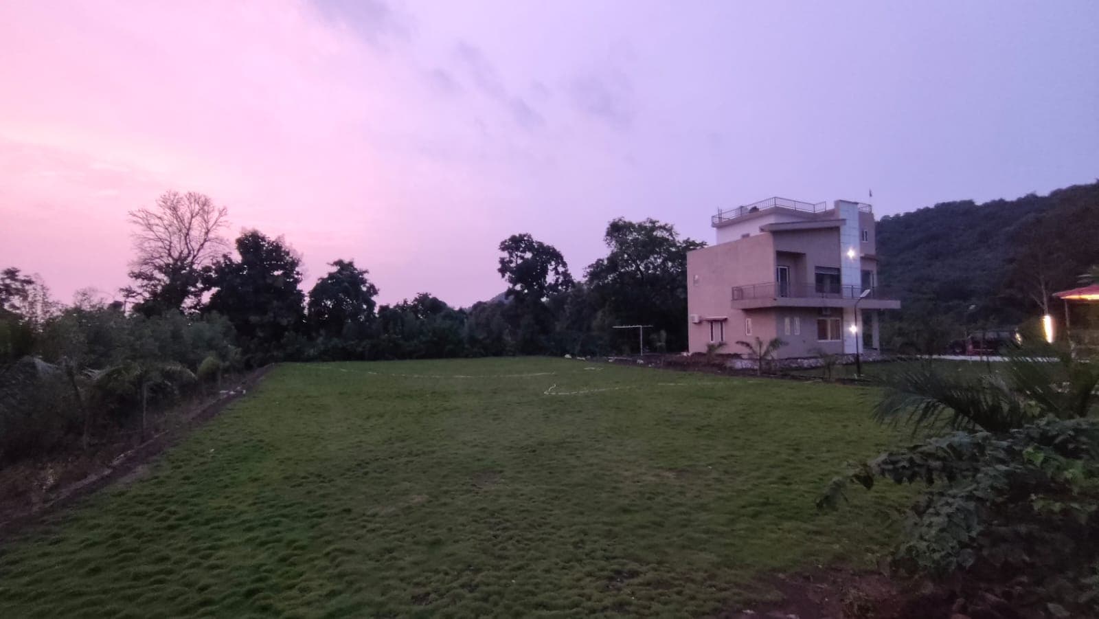 Saanjh at dusk, lawn in front and hills behind.