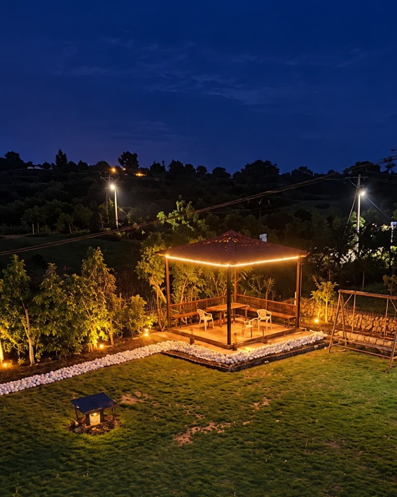 The gazebo lit at night, with the dark hill behind the lawn.