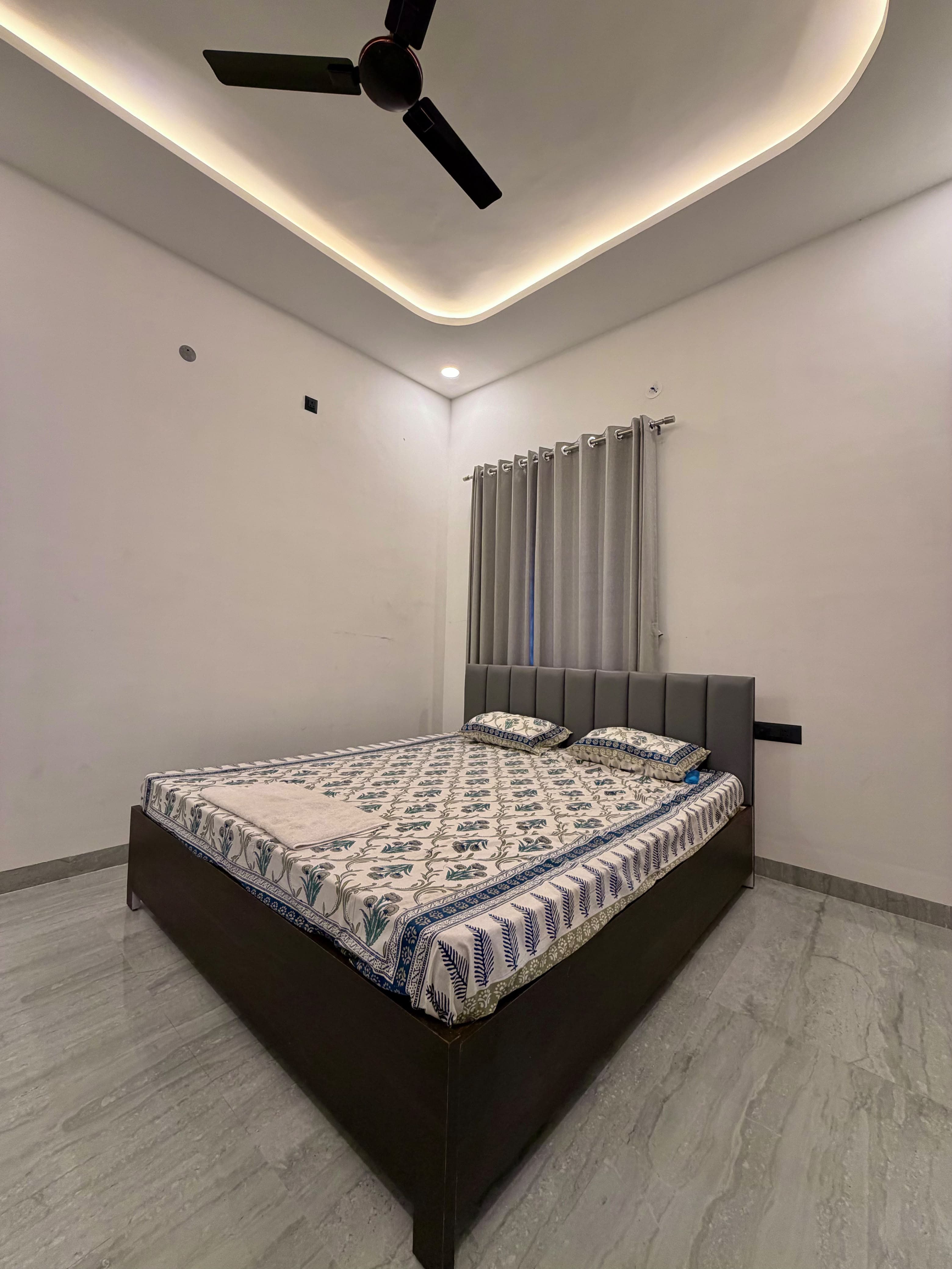 Neel bedroom with comfortable double bed, upholstered headboard, and ambient cove lighting.