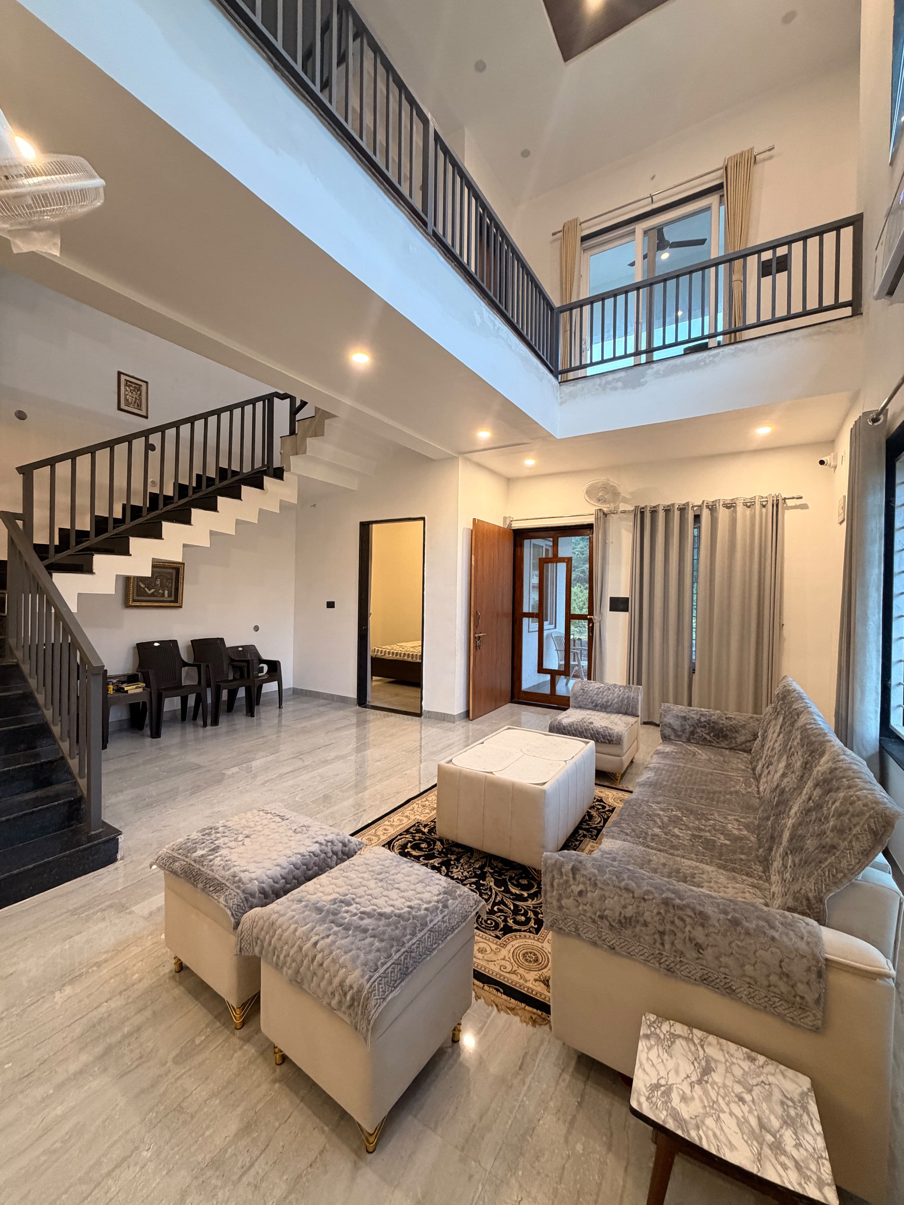 The double-height living room at Saanjh featuring an open mezzanine gallery, architectural staircase, and plush seating.